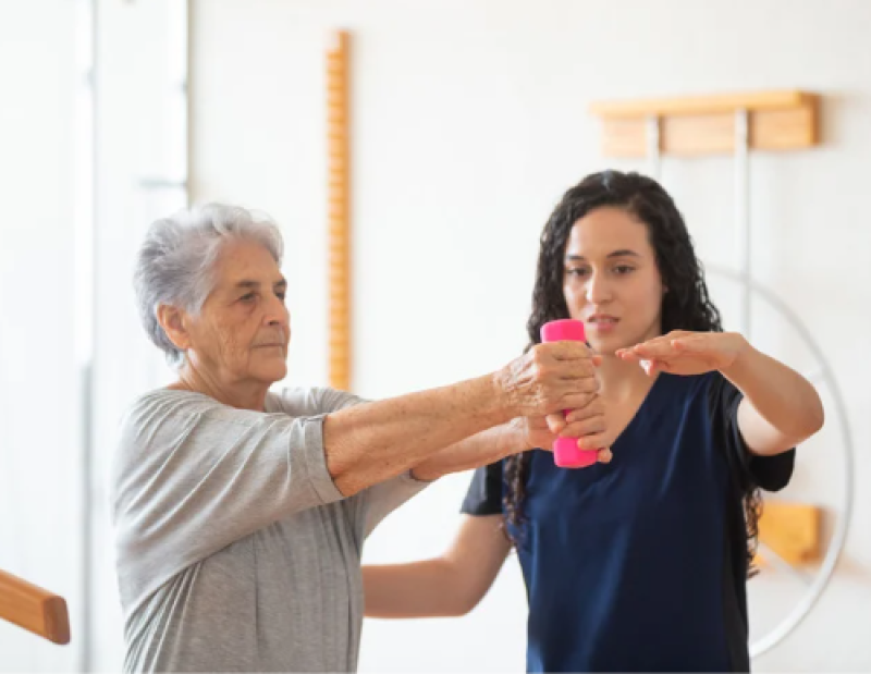 Patient holding a weight which a physical therapist helps her.