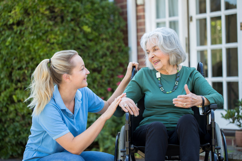 A nurse kneeling next to a resident sitting in a wheel chair.