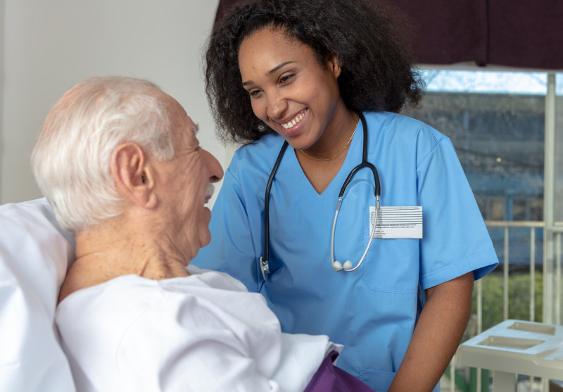 Resident sitting in hospital bed and talking to nurse.