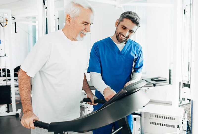 Resident walking on a treadmill with a nurse assisting him.