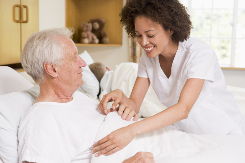 Nurse helping resident in hospital bed.