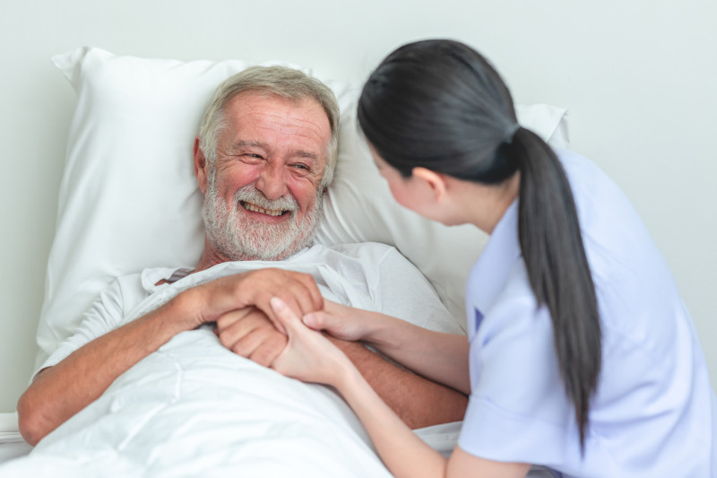 Nurse holding hands with a resident in a hospital bed.