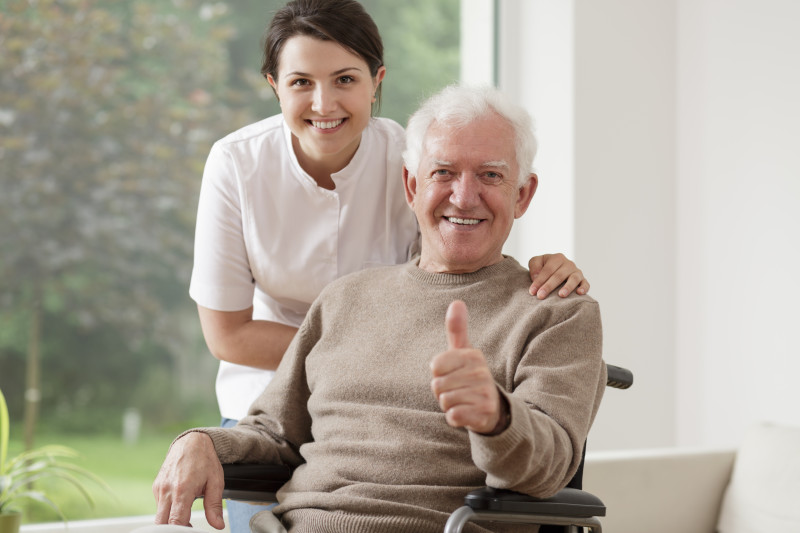 Picture of nurse with her hands on the shoulders of a resident while he holds up a thumbs up.