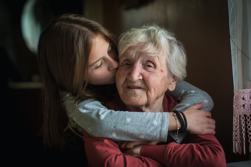 Young girl hugging an elderly woman from behind.
