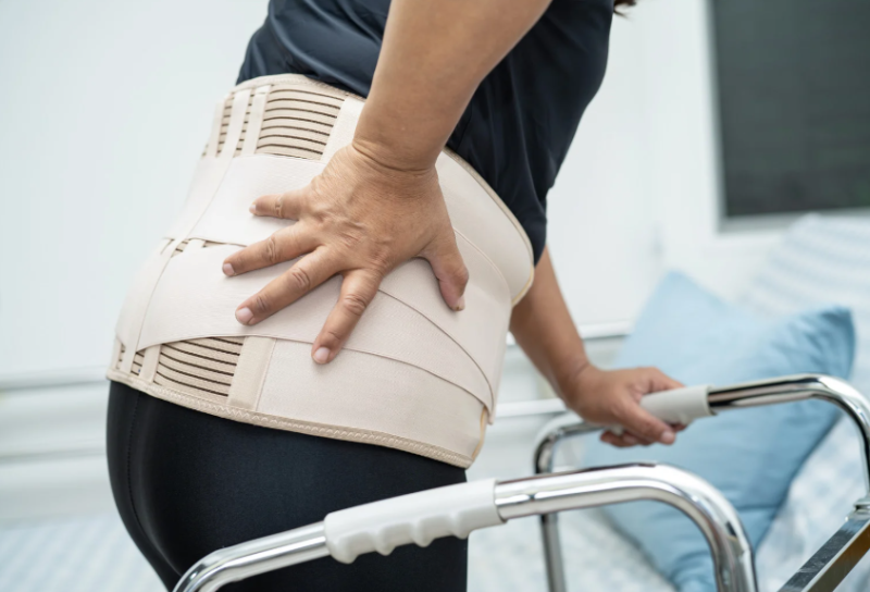 Patient wearing a back brace holding their back.