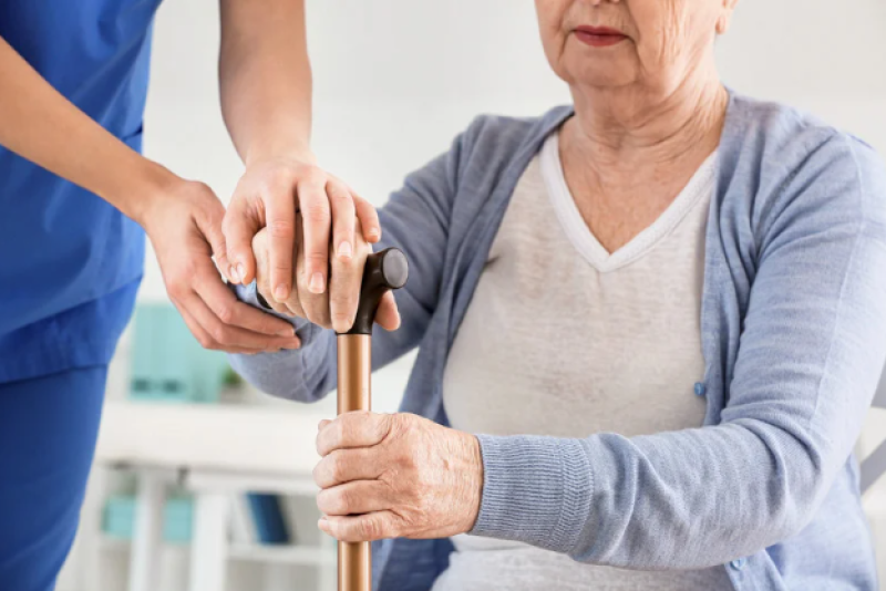 Nurse holding a patients hand to a cane.